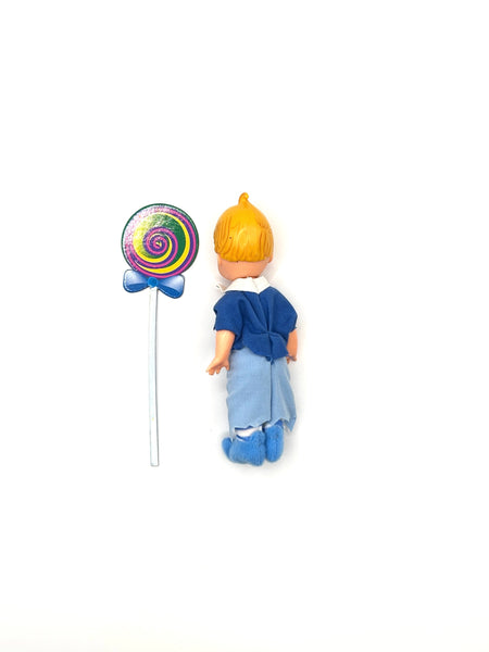 Vintage 1999 Mattel Barbie Kelly Club Wizard of Oz Tommy as Lollipop Munchkin doll next to a colorful swirling rainbow lollipop accessory on a white background