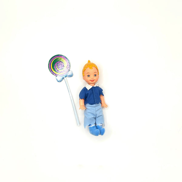 Vintage 1999 Mattel Barbie Kelly Club Wizard of Oz Tommy as Lollipop Munchkin doll next to a colorful swirling rainbow lollipop accessory on a white background