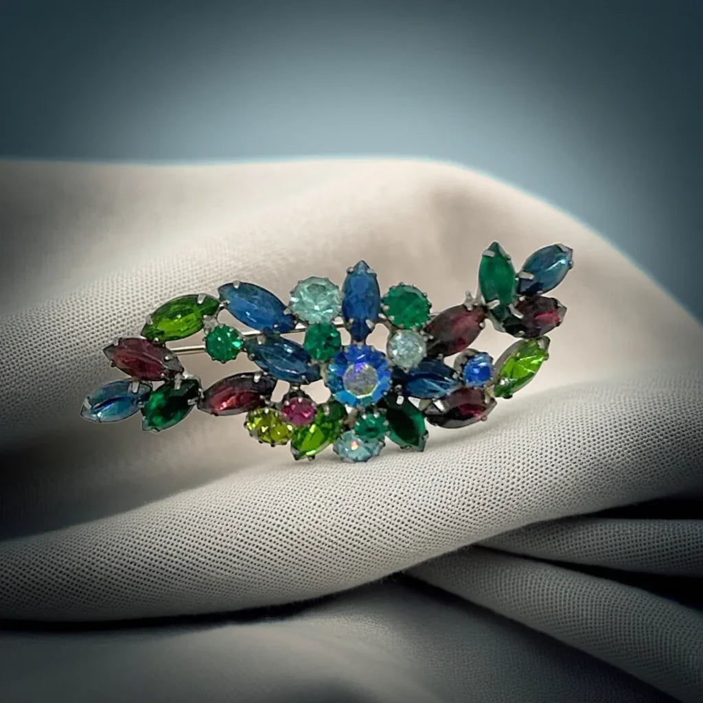 Allow your style to shine with this breathtaking vintage brooch. The stunning combination of marquise stones in varying shades of blue and green, accented by splashes of purple, create a mesmerizing display. Expertly set in silver tone metal with an elegant domed design, this brooch perfectly showcases the beauty and brilliance of each stone.