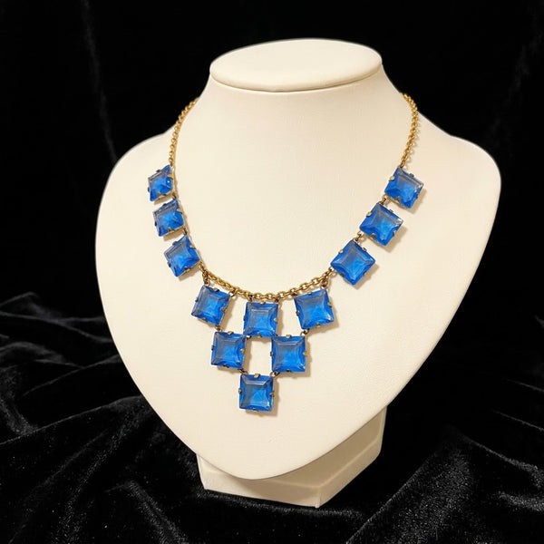Experience the height of sophistication with this exquisite vintage Art Deco necklace. Featuring a flawless line of rich azure square stones, delicately connected by two additional rows, all set on a luxurious gold tone link chain.