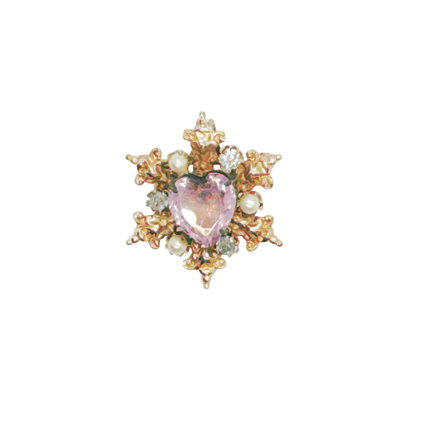 A gold-toned brooch with a central heart-shaped, light purple gemstone. The brooch is surrounded by ornate gold filigree, small pearls, and clear crystals, creating a vintage, elegant design.