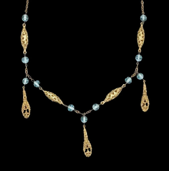 This is a beautiful antique drop necklace, made of golden filigree beads interspersed with clear blue glass accent beads, and punctuated by flat abstract filigree drops. It measures approximately 32" inches long, and the filigree beads each measure about 1”