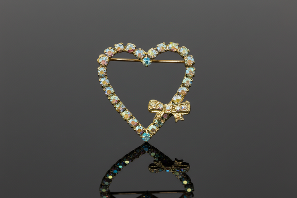 A charming mid-century treasure from the 1940s-50s, this whimsical sweetheart bow pin captures all the romance of vintage style. Crafted from early celluloid plastic, it showcases a playful "Heart Within a Heart" design—a red bow crowning a white heart outline with a dangling red heart that swings freely below.