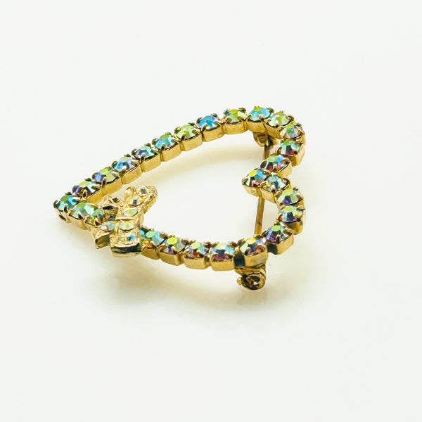 This charming mid-century brooch captures all the sparkle and romance of vintage glamour. The delicate gold-tone heart showcases shimmering aurora borealis rhinestones that dance with rainbow fire, while a sweet bow accent adds an extra touch of whimsy.