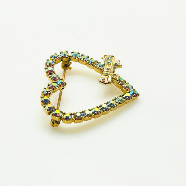 This charming mid-century brooch captures all the sparkle and romance of vintage glamour. The delicate gold-tone heart showcases shimmering aurora borealis rhinestones that dance with rainbow fire, while a sweet bow accent adds an extra touch of whimsy.