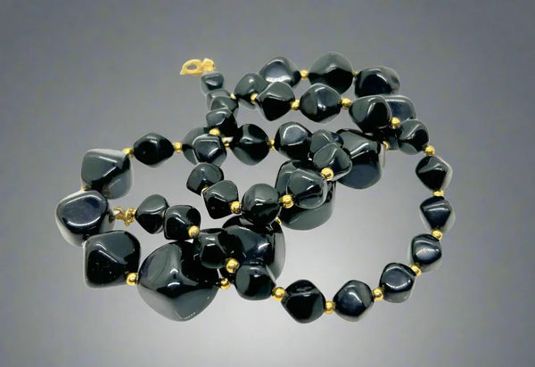 Crafted in 1986, this vintage Avon necklace features a graceful chain of graduated, asymmetrical black beads separated by gold-tone bead separators. Its spring clasp is signed “Avon” in block letters. This exquisite piece measures 24” long, complementing black or solid-color outfits while providing a bold foundation for contrasting accessories.