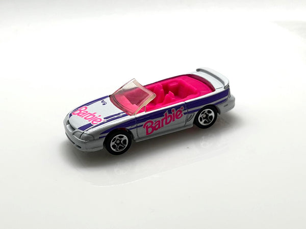 Hot Wheels Barbie 1996 Ford Mustang GT convertible, featuring a silver exterior with purple and pink branding.