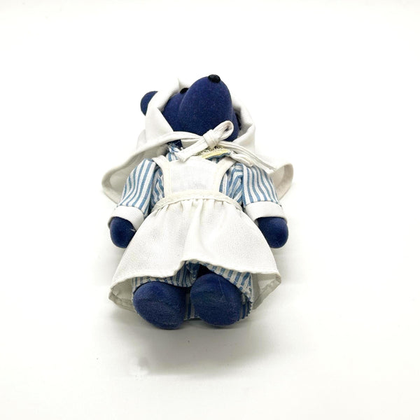 A small plush teddy bear doll wearing a white apron over a blue-and-white striped shirt, photographed against a plain white background.