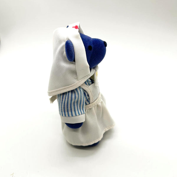 A small plush bear dressed as a nurse, featuring a blue body, a white nurse hat with a tiny red cross, and a blue-and-white striped shirt, photographed on a plain white background.