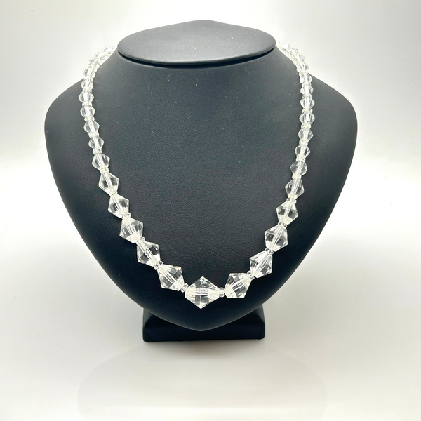 A clear faceted crystal bead necklace displayed on a matte black jewelry bust against a white studio background.