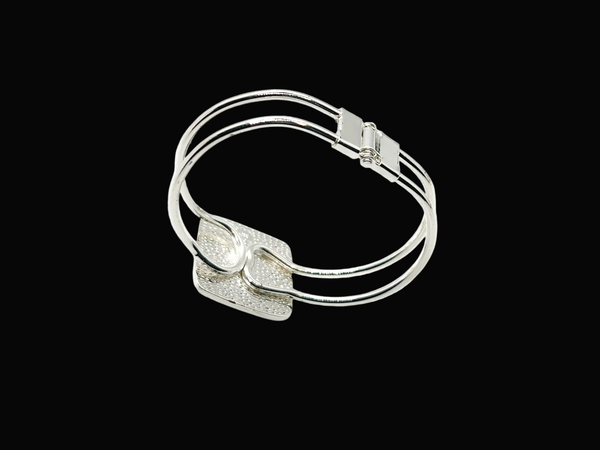 This striking vintage bracelet showcases a bold black square onyx stone set in polished silver. The architectural design features dual silver bands converging at the center stone with a hinged hook-bangle closure for easy wear. 