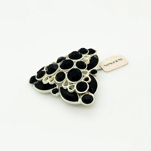 This is a highly unusual vintage brooch made of a white enamel frame and set with black faceted stones. It still retains the store tag. 