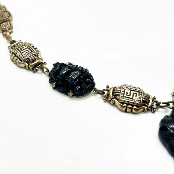 An Art Deco choker necklace with gold-tone filigree links and three dark, intricately carved floral beads, featuring a larger central pendant drop