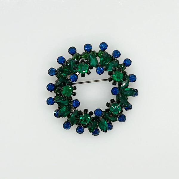 This stunning brooch features a dazzling mix of blue and green rhinestones in round and marquise cuts, all set in blackened metal for a striking layered effect. Its eye-catching design is complemented by excellent condition and the distinctive figure 8 markings on the back, suggesting it’s an unsigned Juliana piece. Measuring 2 inches wide, this unique accessory is perfect for adding vintage charm to any outfit. Enjoy Free Shipping with your purchase.