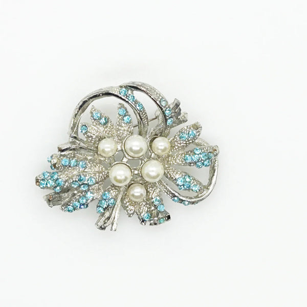 With a touch of elegance, this vintage brooch boasts delicate power blue rhinestones accented by six lustrous faux pearls of different sizes.