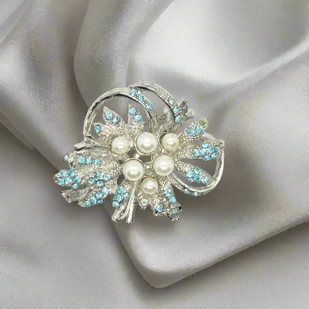 This exquisite vintage brooch showcases dazzling power blue rhinestones that catch the light beautifully, complemented by six lustrous faux pearls in assorted sizes for added dimension and elegance. Expertly set against a textured silvertone metal backing, the pin measures 1.75 inches wide, making it a perfect statement piece that enhances both casual and formal attire