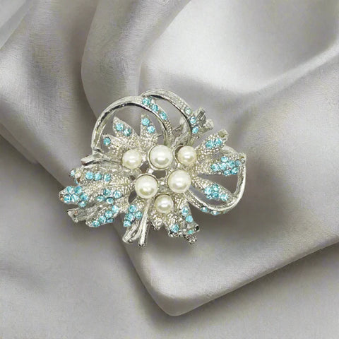 This exquisite vintage brooch showcases dazzling power blue rhinestones that catch the light beautifully, complemented by six lustrous faux pearls in assorted sizes for added dimension and elegance. Expertly set against a textured silvertone metal backing, the pin measures 1.75 inches wide, making it a perfect statement piece that enhances both casual and formal attire