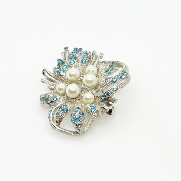 With a touch of elegance, this vintage brooch boasts delicate power blue rhinestones accented by six lustrous faux pearls of different sizes.