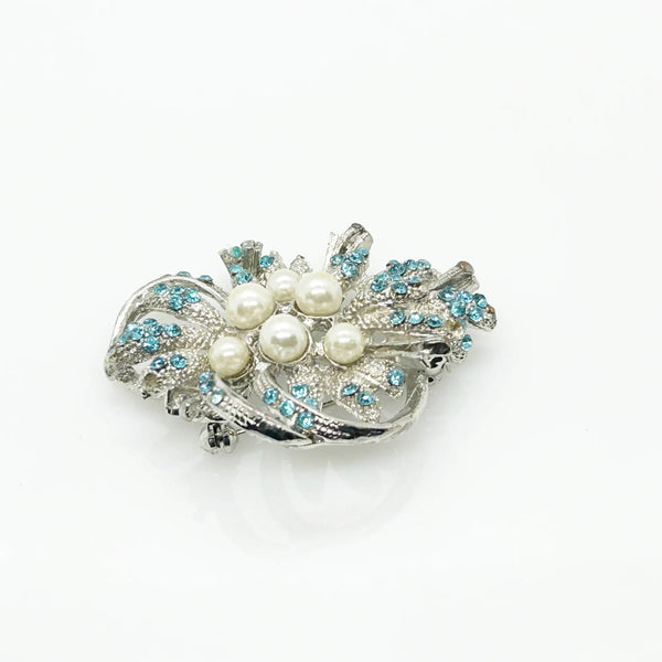 With a touch of elegance, this vintage brooch boasts delicate power blue rhinestones accented by six lustrous faux pearls of different sizes.