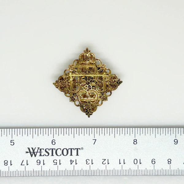 This exquisite brooch with an Old World aesthetic showcases finely crafted gold filigree petals encircling a square stone in elegant blue-purple tones. Between each delicate petal rests a round, iridescent stone that complements the central hues, adding subtle depth and shimmer. 