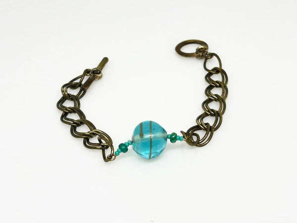 This captivating vintage bracelet boasts two rows of links on either side of a stunning blue glass marble with shimmering gold stripes. It is 7 1/2" in length and features a charming toggle clasp