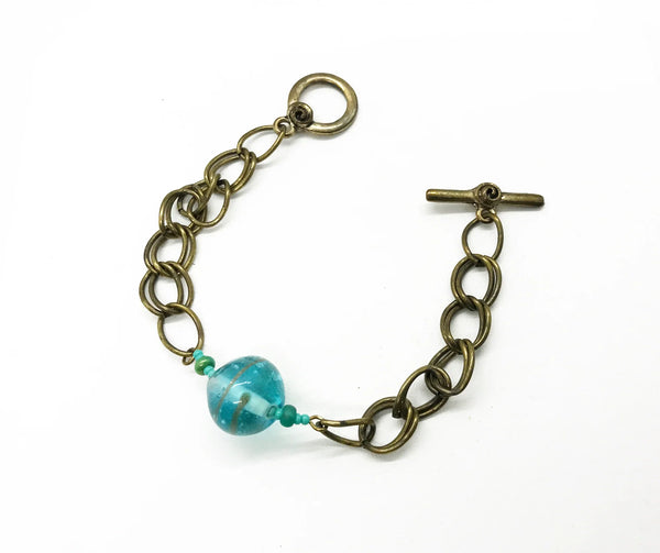 This captivating vintage bracelet boasts two rows of links on either side of a stunning blue glass marble with shimmering gold stripes. It is 7 1/2" in length and features a charming toggle clasp