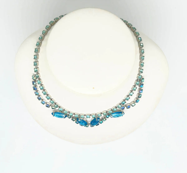 This exquisite brooch with an Old World aesthetic showcases finely crafted gold filigree petals encircling a square stone in elegant blue-purple tones. Between each delicate petal rests a round, iridescent stone that complements the central hues, adding subtle depth and shimmer.