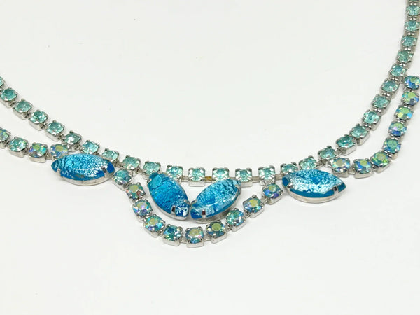 This exquisite brooch with an Old World aesthetic showcases finely crafted gold filigree petals encircling a square stone in elegant blue-purple tones. Between each delicate petal rests a round, iridescent stone that complements the central hues, adding subtle depth and shimmer.