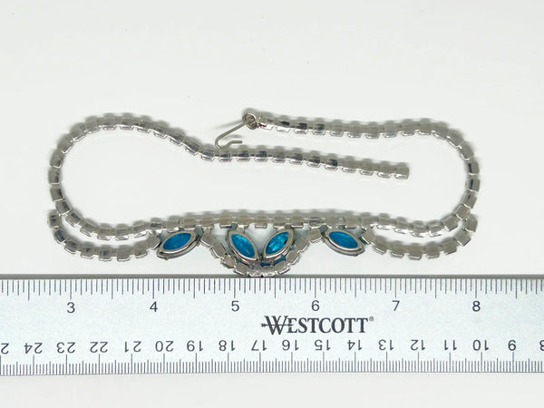 This exquisite brooch with an Old World aesthetic showcases finely crafted gold filigree petals encircling a square stone in elegant blue-purple tones. Between each delicate petal rests a round, iridescent stone that complements the central hues, adding subtle depth and shimmer.