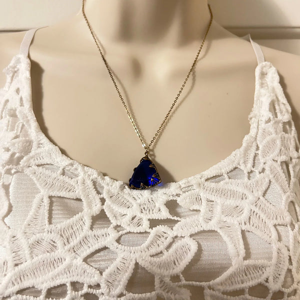 This extraordinary art deco pendant necklace is fashioned from a triangular, faceted piece of cobalt blue glass that measures 3/4" on each side. It also includes a spring clasp chain that is 18" long. The necklace is in excellent condition and has a captivating blue violet hue that is complemented by an uncommon cut