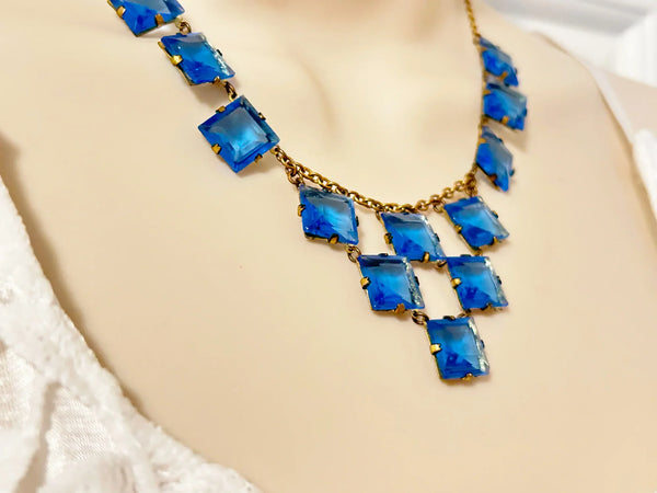 Experience the height of sophistication with this exquisite vintage Art Deco necklace. Featuring a flawless line of rich azure square stones, delicately connected by two additional rows, all set on a luxurious gold tone link chain. The stones are meticulously held in place with thin claw settings, revealing their exposed backs for an added touch of elegance.