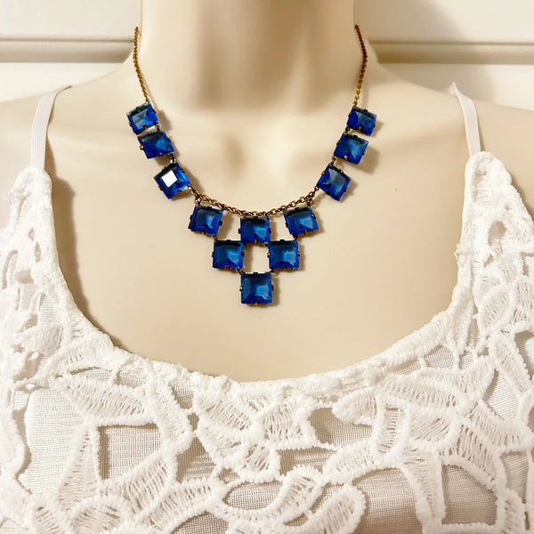 Experience the height of sophistication with this exquisite vintage Art Deco necklace. Featuring a flawless line of rich azure square stones, delicately connected by two additional rows, all set on a luxurious gold tone link chain. The stones are meticulously held in place with thin claw settings, revealing their exposed backs for an added touch of elegance.