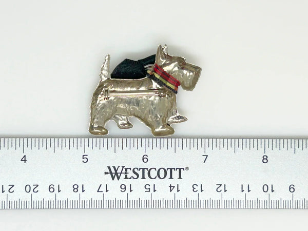 This vintage brooch features a dapper terrier dog with a black velvet bow and plaid collar, expertly crafted in silver tone metal. It measures 2" wide, in excellent condition. This brooch will add some pizzazz to your outfit! Featuring a stylish terrier pup adorned with a black velvet bow and plaid collar, this quirky piece is expertly crafted, and it's in excellent condition - what a steal!