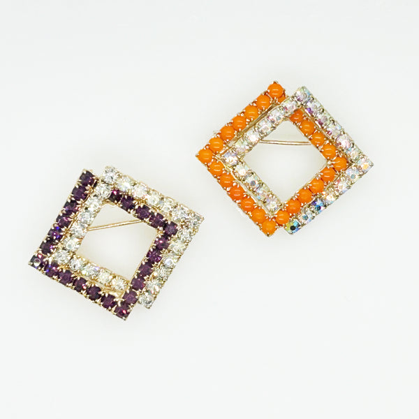 Set of two vintage 3D interlocking square brooches. One features purple and clear prong-set rhinestones on a silver-tone frame. The other features opaque orange and sparkling gold AB crystals on a gold-tone geometric frame