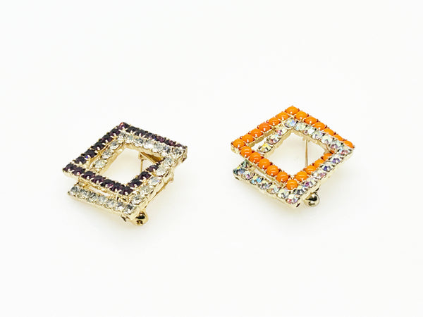 Set of two vintage 3D interlocking square brooches. One features purple and clear prong-set rhinestones on a silver-tone frame. The other features opaque orange and sparkling gold AB crystals on a gold-tone geometric frame