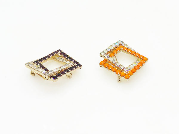 Set of two vintage 3D interlocking square brooches. One features purple and clear prong-set rhinestones on a silver-tone frame. The other features opaque orange and sparkling gold AB crystals on a gold-tone geometric frame