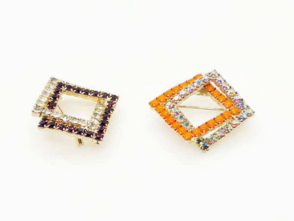 Set of two vintage 3D interlocking square brooches. One features purple and clear prong-set rhinestones on a silver-tone frame. The other features opaque orange and sparkling gold AB crystals on a gold-tone geometric frame