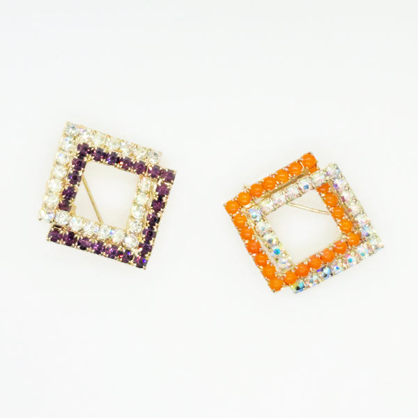 Set of two vintage 3D interlocking square brooches. One features purple and clear prong-set rhinestones on a silver-tone frame. The other features opaque orange and sparkling gold AB crystals on a gold-tone geometric frame