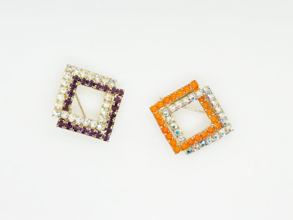 Set of two vintage 3D interlocking square brooches. One features purple and clear prong-set rhinestones on a silver-tone frame. The other features opaque orange and sparkling gold AB crystals on a gold-tone geometric frame