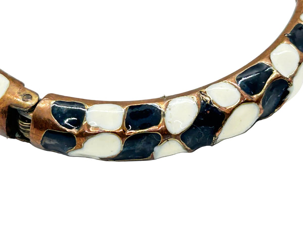 This striking hinge bangle bracelet showcases bold geometric patterns rendered in contrasting black and white enamel, accented with warm copper metalwork. The repeating abstract design creates visual interest from every angle, making it a versatile piece that complements both casual and dressed-up looks