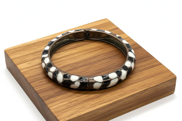 This striking hinge bangle bracelet showcases bold geometric patterns rendered in contrasting black and white enamel, accented with warm copper metalwork. 
