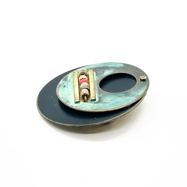 Intriguing modernist brooch with layered circular components, including a dark, possibly rubber or ebonized material, and a verdigris-patinated or painted metal plate.