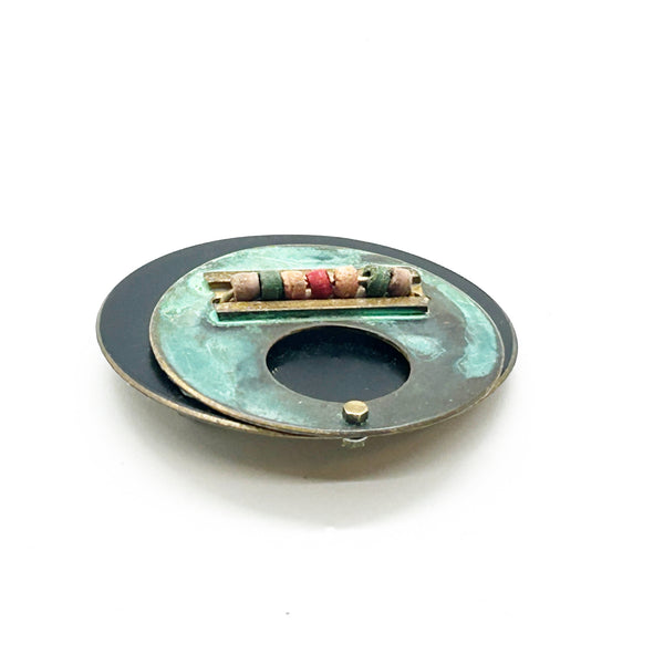 Intriguing modernist brooch with layered circular components, including a dark, possibly rubber or ebonized material, and a verdigris-patinated or painted metal plate.