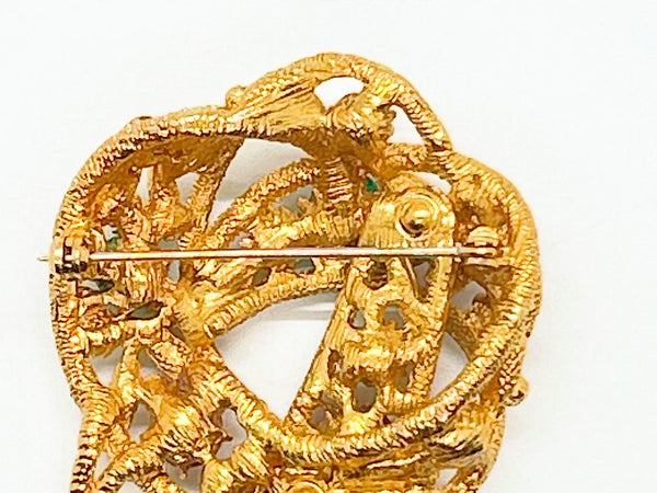 An image showing the reverse side of a textured gold-tone vintage costume jewelry brooch. The brooch is shaped like a textured, openwork abstract ribbon loop or bow with a dangling end pointing downward. A long, horizontal metal pin stem and safety clasp run across the upper back portion. On the lower section of the brooch, an oval cartouche containing the Capri maker's mark is stamped directly onto the textured filigree-style metal framework
