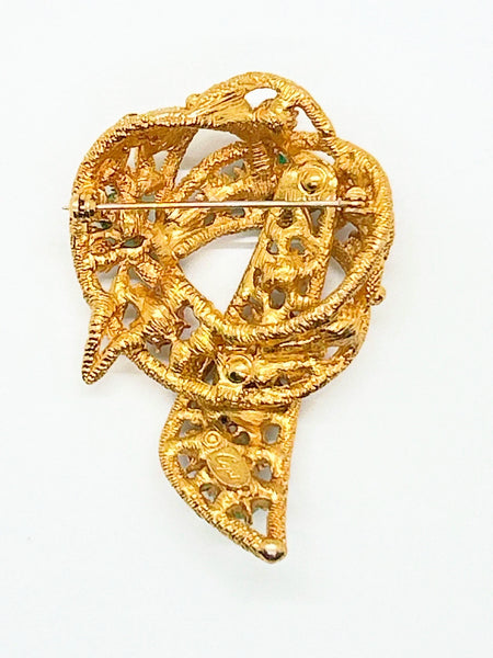 An image showing the reverse side of a textured gold-tone vintage costume jewelry brooch. The brooch is shaped like a textured, openwork abstract ribbon loop or bow with a dangling end pointing downward. A long, horizontal metal pin stem and safety clasp run across the upper back portion. On the lower section of the brooch, an oval cartouche containing the Capri maker's mark is stamped directly onto the textured filigree-style metal framework