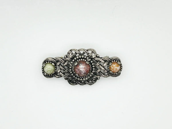 Embellish your style with the elegant and enduring Vintage Celtic Knot Style Brooch Art Glass. This beautifully crafted brooch features textured metal encasing stunning round stones in shades of pale green, red, and gold-amber. Measuring at 1.75", this accessory will add a touch of sophistication to any ensemble. Perfect for those seeking a refined and timeless addition to their collection.