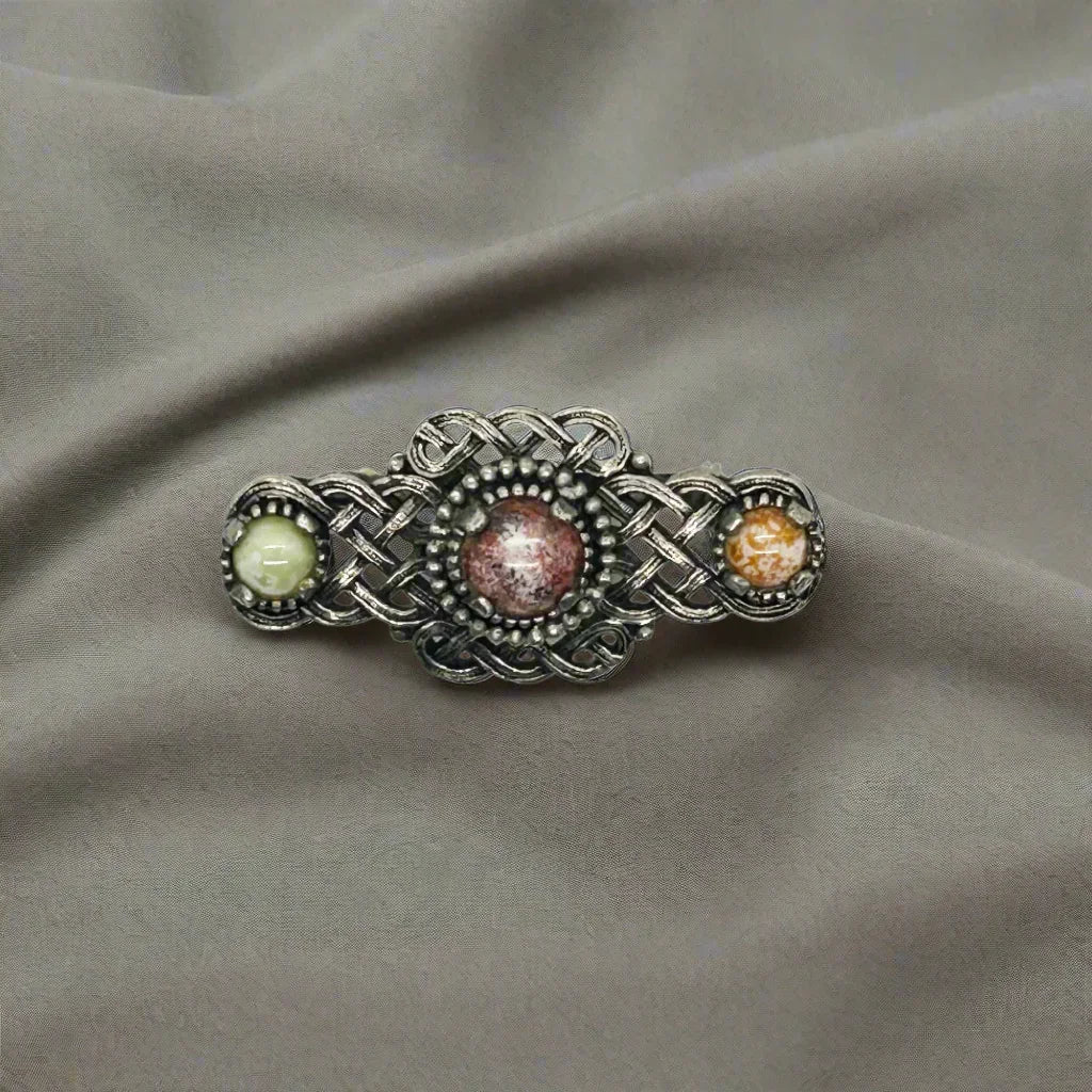Embellish your style with the elegant and enduring Vintage Celtic Knot Style Brooch Art Glass. This beautifully crafted brooch features textured metal encasing stunning round stones in shades of pale green, red, and gold-amber.