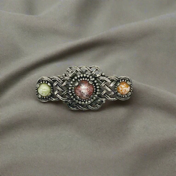Embellish your style with the elegant and enduring Vintage Celtic Knot Style Brooch Art Glass. This beautifully crafted brooch features textured metal encasing stunning round stones in shades of pale green, red, and gold-amber.