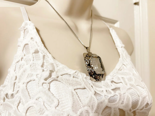 Encased on a silver rectangular frame, this clear rectangular glass pendant is bezel set and exudes timeless charm;It is mounted in a silver rectangular frame adorned with a garland. Measuring 1.75 inches in height and 1.25 inches across, it is a substantial piece that will make a statement. 