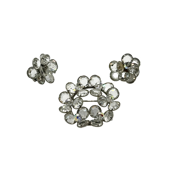 A matching vintage 1950s rhinestone demi parure jewelry set featuring a layered circular brooch and a pair of small flower cluster clip-on earrings, arranged neatly on a clean white background.